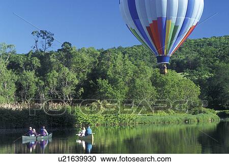 Stock Image -  hot air balloon, canoeing, Vermont, VT, Quechee, People canoeing in a pond watch a hot air balloon float above at the Quechee Hot Air Balloon Festival.. Fotosearch