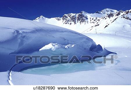 Stock Image -  ice, snow, mountains, Alps, Switzerland, Valais, Les Crosets, Portes du Soleil, Swiss Alps, Europe, Turquoise colored ice forms on a pond high in the Swiss Alps in the winter.. Fotosearch