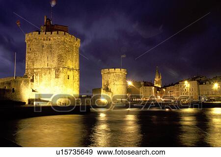Stock Photo -  La Rochelle, France, Poitou-Charentes, Charente-Maritime, Europe, 14th century medieval stone towers illuminated at night at the entrance to the harbor of the ancient fortified old port city of La Rochelle on the Atlantic Ocean.. Fotosearch