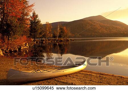 Stock Photography -  lake, canoe, Adirondacks, New York, Blue Mountain Lake, NY, A canoe rests on a quiet beach on the calm waters of Blue Mountain Lake in the autumn in the Adirondacks.. Fotosearch