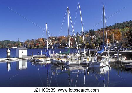 Stock Photo -  marina, Sunapee, NH, New Hampshire, Sailboats moored at a dock on the calm waters of Lake Sunapee in Sunapee in the autumn.. Fotosearch