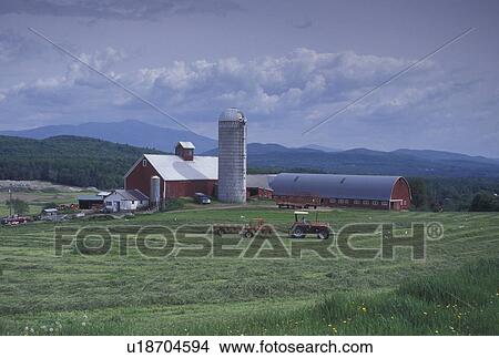 Picture -  red barn, farm, spring, Mt. Mansfield, Fletcher, VT, Vermont, Tractor raking hay in a field on Tinker Farm in Fletcher in the spring. Scenic view of Mount Mansfield in the background.. Fotosearch