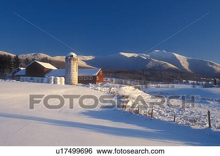 Stock Photograph -  red barn, farm, winter scene, mountain, winter, Mt. Mansfield, Scenic view of the snow covered Mount Mansfield and a red barn on a farm on a sunny day in the winter in Cambridge in Lamoille County in the state of Vermont. . Fotosearch
