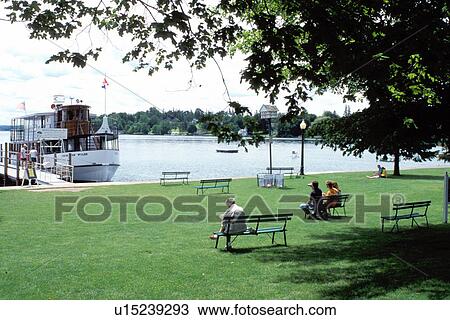 Stock Image -  Skaneateles, NY, New York, Finger Lakes, Public park and cruise boat on Skaneateles Lake.. Fotosearch