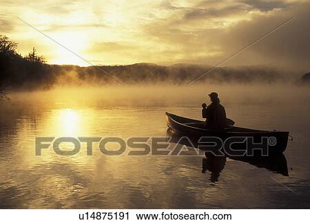Stock Image -  sunrise, canoeing, sunset, canoe, Vermont, VT, Woman paddling a canoe on Mollys Falls Pond at sunrise in the mist.. Fotosearch