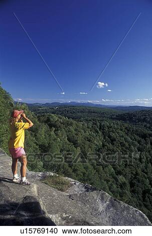 Stock Image -  Vermont, VT, Woman looking through binoculars on Nichols Ledge in Woodbury . Fotosearch