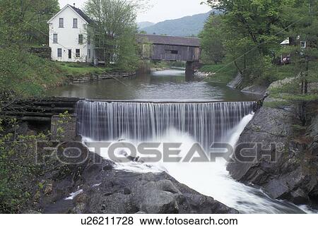 Stock Photo -  waterfall, covered bridge, dam, spring, Warren, VT, Vermont, Warren Covered Bridge crosses the Mad River with a waterfall in the foreground in Warren in the Mad River Valley in the spring. . Fotosearch