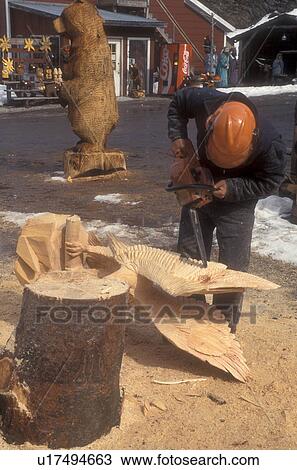 Stock Image -  wood carving, chain saw, sculpture, woodwork, Man carves large wooden figures using a chainsaw at the Spinning Wheel Gift Shop in Stowe in Lamoille County in the state of Vermont.. Fotosearch