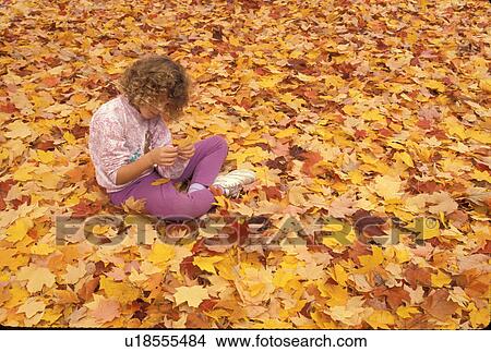 Young girl sitting alone on the ground full of colorful red, orange, yellow, maple leaves, fall leaves. Girl is looking at leaf. View Large Photo Image Picture - Young girl sitting alone on the ground full of colorful red, orange, yellow, maple leaves, fall leaves. Girl is looking at leaf.. Fotosearch