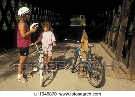 Stock Image -  biking, safety, Stone Mountain, GA, Atlanta, Georgia, Mother helping 8 year old daughter to put on her bike helmet at Georgia's Stone Mountain Park in Stone Mountain. . Fotosearch