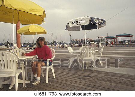 Stock Image -  cafT, Daytona Beach, FL, Florida, Atlantic Ocean, Woman sitting at an outdoor cafT on the pier on Halifax Harbor in Daytona Beach.. Fotosearch