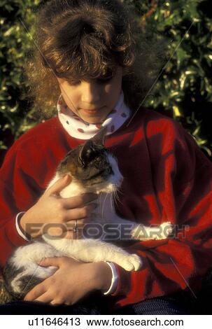Stock Image -  cat, girl, Young nine year old girl with red sweatshirt cuddles her cat in her arms in Atlanta, GA.. Fotosearch