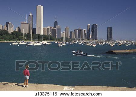 Stock Photography -  Chicago, IL, Illinois, Lake Michigan, skyline, Woman watching a boat in the Chicago Harbor from Grant Park with a view of the downtown skyline of Chicago. . Fotosearch