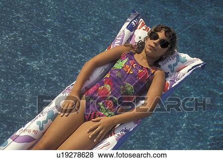 Stock Photo -  girl, swimming, pool, 8 year old girl with sun glasses in a bathing suit lying on her back on a float in a swimming pool.. Fotosearch