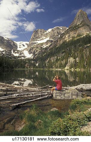 Stock Image -  hiking, Rocky Mountains National Park, Rocky Mountains, CO, Colorado, Woman sitting on a boulder looking with binoculars at Odessa Lake in Rocky Mountain National Park.. Fotosearch