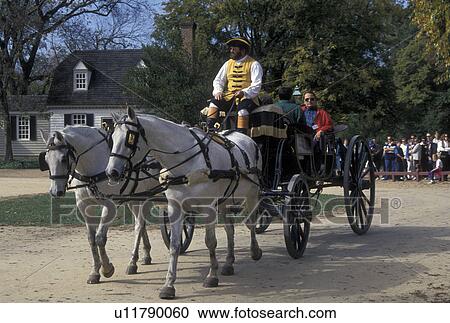 Stock Image -  horse-drawn carriage, Colonial Williamsburg, VA, Williamsburg, Virginia, A team of horses pulling an open carriage carries tourists through the 18th century village of Colonial Williamsburg in Colonial Williamsburg Historic Area.. Fotosearch