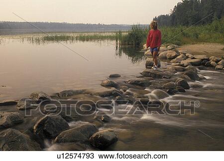 Stock Image -  Itasca State Park, Mississippi River, MN, Minnesota, Park Rapids, Lake Itasca, A woman walks across the narrow headwaters of the Mississippi River on large rocks in Itasca State Park.. Fotosearch