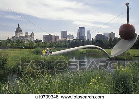 Stock Photograph -  Minneapolis, MN, cherry, spoon, skyline, Minnesota, Twin Cities, Spoon Bridge and Cherry Sculpture In the Minneapolis Sculpture Garden at Walker Art Center in Minneapolis. View of the downtown skyline of Minneapolis in the background.. Fotosearch