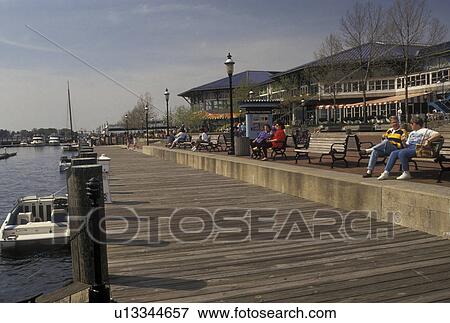 Stock Photo -  Norfolk, Hampton Roads Area, VA, Virginia, People sitting on park benches along the pier at The Waterside along the Elizabeth River in Norfolk in the spring.. Fotosearch