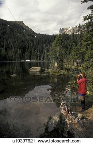 Stock Image -  Rocky Mountain National Park, CO, Colorado, Woman taking pictures of the scenic Fern Lake in Rocky Mountain Nat'l Park.. Fotosearch