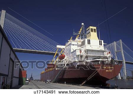 Stock Image -  Savannah, GA, Georgia, A cargo ship is moored at the Dock Yard in Savannah. Talmadge Memorial Bridge crosses the Savannah River.. Fotosearch