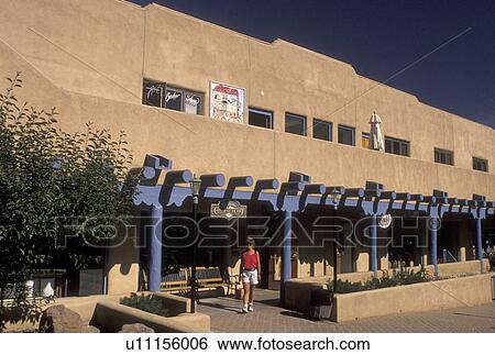 Stock Photograph -  shops, Taos, NM, New Mexico, Woman walking out of a shopping plaza, adobe style architecture, in the village of Taos.. Fotosearch