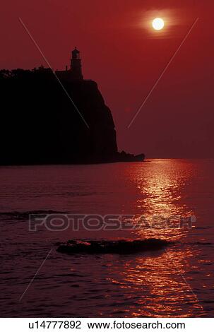 Stock Image -  sunrise, lighthouse, Lake Superior, North Shore Drive, Two Harbors, MN, Minnesota, The sun rises behind Split Rock Lighthouse which is situated on a high cliff on the north shore of Lake Superior at Split Rock Lighthouse State Park in Two Harbors. Red fi. Fotosearch