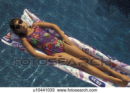 Stock Image -  swimming, pool, girl, 8 year old girl with sun glasses in a bathing suit lying on her back on a float in a swimming pool.. Fotosearch