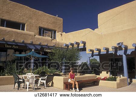 Taos, NM, New Mexico, Woman sitting on a bench next to an outdoor cafT in a shopping plaza, adobe style architecture, in the village of Taos. View Large Photo Image Stock Photo - Taos, NM, New Mexico, Woman sitting on a bench next to an outdoor cafT in a shopping plaza, adobe style architecture, in the village of Taos.. Fotosearch