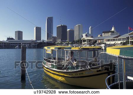 Stock Photo -  water taxi, skyline, Miami, FL, Florida, Atlantic Ocean, Yellow water taxi docked outside Bayside Marketplace, a shopping, dining, entertainment mecca, on Biscayne Bay and skyline of downtown Miami.. Fotosearch