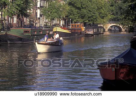 Stock Image -  Amsterdam, Netherlands, Holland, Noord-Holland, Europe, Boat cruises down a canal in Amsterdam.. Fotosearch