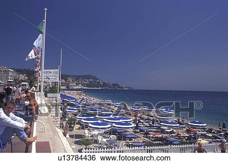 beach, France, Nice, Cote d' Azur, Provence, Alpes-Maritimes, Europe, People sitting along the Promenade des Anglais watching the beach filled with sunbathers and blue beach umbrellas on the Mediterranean Sea in the city of Nice. View Large Photo Image Stock Photograph - beach, France, Nice, Cote d' Azur, Provence, Alpes-Maritimes, Europe, People sitting along the Promenade des Anglais watching the beach filled with sunbathers and blue beach umbrellas on the Mediterranean Sea in the city of Nice.. Fotosearch