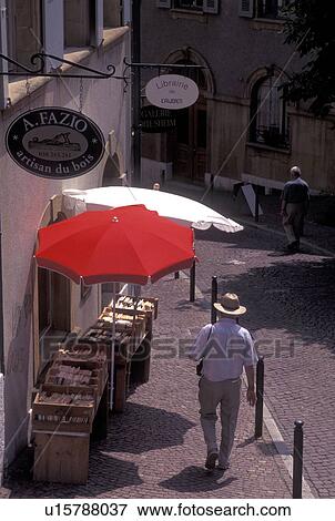 Stock Photo -  book store, Switzerland, Neuchatel, Man walks by a display of books for sale under red and white umbrellas outside a bookstore along a cobblestone pedestrian street in downtown Neuchatel.. Fotosearch