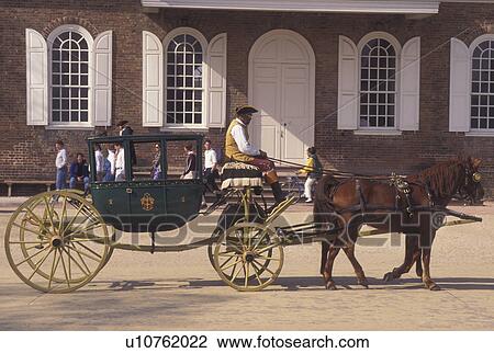 Stock Image -  Colonial Williamsburg, horse-drawn carriage, Williamsburg, VA, Virginia, A team of horses pulling a covered carriage passes by the Courthouse in the 18th century village of Colonial Williamsburg in Colonial Williamsburg Historic Area.. Fotosearch