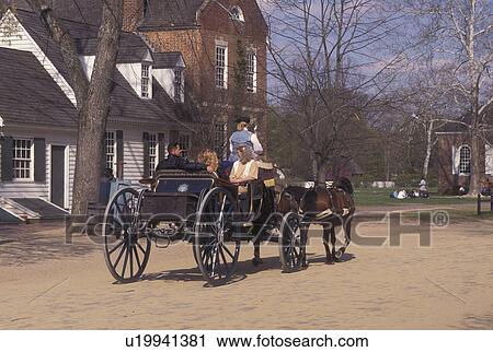 Stock Image -  Colonial Williamsburg, VA, horse-drawn carriage, Williamsburg, Virginia, A team of horses pulling an open carriage carries tourists through the 18th century village of Colonial Williamsburg in Colonial Williamsburg Historic Area.. Fotosearch