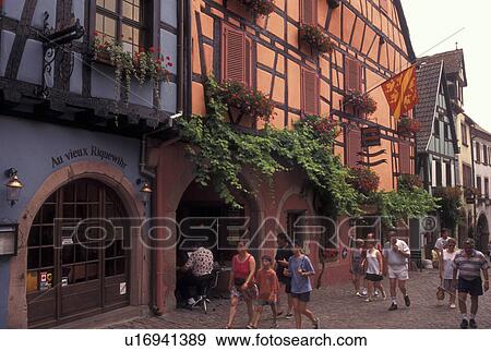 Stock Photo -  France, Alsace, Riquerwihr, Haut-Rhin, Europe, wine region, People walking on the cobbled streets surrounded by half-timbered buildings in the picturesque village of Riquerwihr in the wine region of Alsace.. Fotosearch