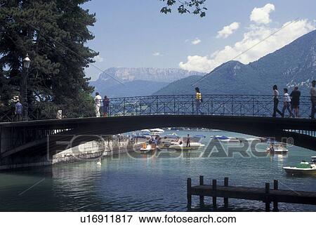 Stock Photo -  France, Annecy, Haute-Savoie, Rhone-Alpes, Europe, Pedestrian bridge crosses the Vasse canal on scenic Lake Annecy (Lac d' Annecy) surrounded by mountains in Annecy. . Fotosearch