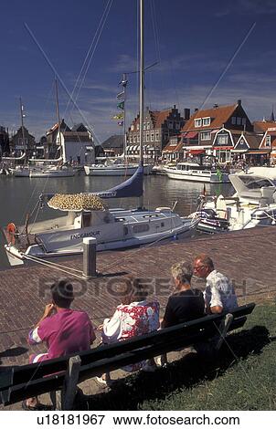 Stock Photo -  Holland, Netherlands, Volendam, Noord-Holland, Europe, People relaxing on a bench on the waterfront on the harbor on Markermeer in the town of Volendam.. Fotosearch
