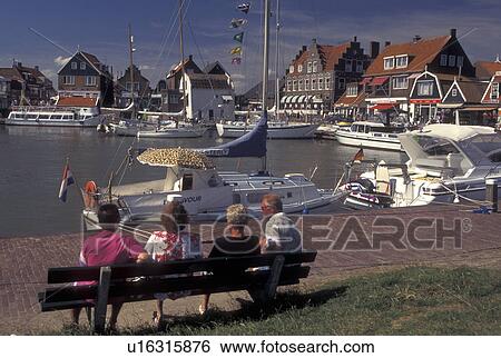 Stock Photograph -  Holland, Volendam, Netherlands, Noord-Holland, Europe, People relaxing on a bench on the waterfront on the harbor on Markermeer in the town of Volendam.. Fotosearch