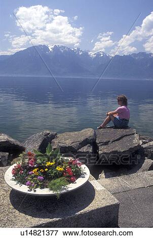 Lake Geneva, Switzerland, Vaud, Vevey, Alps, Woman sitting on a rock looking out at the scenic view of Lac Leman and the Alps from a lakefront park in Vevey in the Canton of Vaud. View Large Photo Image Stock Photo - Lake Geneva, Switzerland, Vaud, Vevey, Alps, Woman sitting on a rock looking out at the scenic view of Lac Leman and the Alps from a lakefront park in Vevey in the Canton of Vaud. . Fotosearch