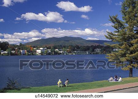 Lake Placid, NY, New York, The Adirondacks, People sitting on the lakefront of Mirror Lake looking at the resort town of Lake Placid in the autumn. View Large Photo Image Stock Image - Lake Placid, NY, New York, The Adirondacks, People sitting on the lakefront of Mirror Lake looking at the resort town of Lake Placid in the autumn.. Fotosearch