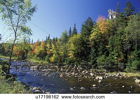 Stock Image -  Lake Placid, NY, New York, The Adirondacks, Scenic Ausable River in Lake Placid in the autumn. Ski Jump at the Olympic Complex in the background.. Fotosearch