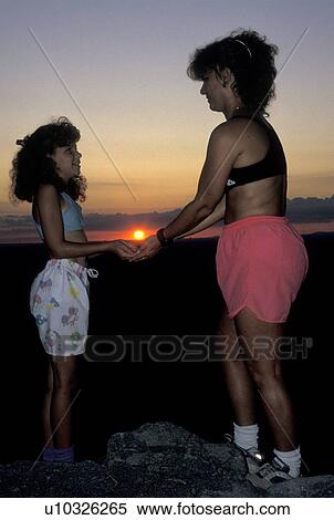 Stock Photography -  mother and daughter, GA, Georgia, Atlanta, Mother and 10 year old daughter stand facing each other holding the sun in their hands on top of Stone Mountain at sunset.. Fotosearch
