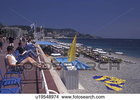 Nice, Cote d' Azur, beach, France, Provence, Alpes-Maritimes, Europe, People sitting along the Promenade des Anglais watching the beach filled with sunbathers and blue and white beach umbrellas on the Mediterranean Sea in the city of Nice. View Large Photo Image Picture - Nice, Cote d' Azur, beach, France, Provence, Alpes-Maritimes, Europe, People sitting along the Promenade des Anglais watching the beach filled with sunbathers and blue and white beach umbrellas on the Mediterranean Sea in the city of Nice.. Fotosearch