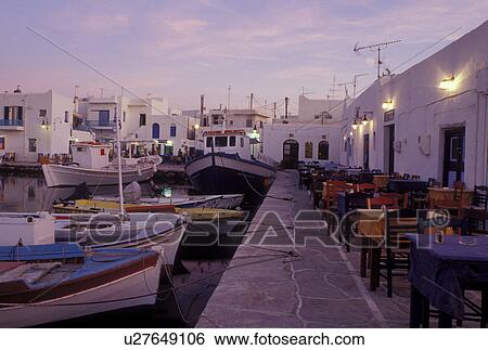 Stock Photograph -  outdoor cafT, Greece, Paros, Naoussa, Greek Islands, Cyclades, Europe, Outdoor cafT along the waterfront and fishing boats docked in Naoussa Harbor in the evening on Paros Island on the Aegean Sea.. Fotosearch