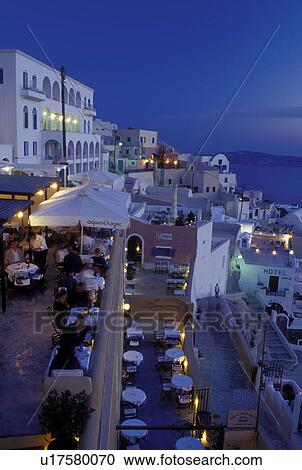 Stock Image -  outdoor cafT, Santorini, Greek Islands, Fira, Cyclades, Greece, Europe, Outdoor restaurants and terraces in the village of Fira in the evening on the steep hillside of Santorini Island overlooking the Aegean Sea.. Fotosearch