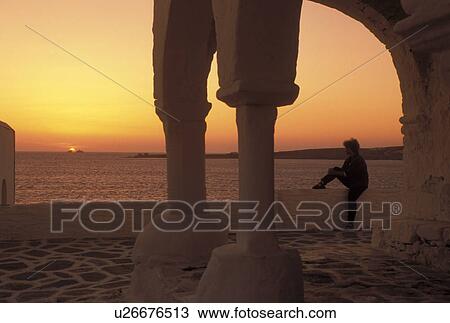 Stock Image -  Paros, Greek Islands, Parikia, Cyclades, Greece, Europe, Woman watching the sunset over the Aegean Sea from the terrace of a whitewashed church in the town of Parikia on Paros Island.. Fotosearch