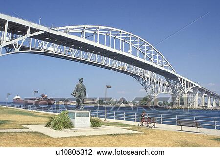 Stock Image -  Port Huron, MI, Lake Huron, Michigan, Thomas Edison Statue below the Blue Water International Bridge which spans the St. Clair River at Port Huron.. Fotosearch