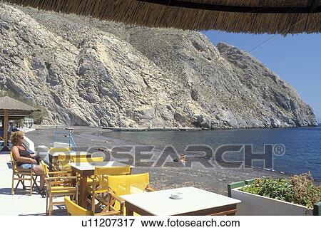Santorini, Greek Islands, Perissa, Cyclades, Greece, Europe, Woman sitting at an outdoor cafT along the black sandy beach of Perissa on the Aegean Sea. View Large Photo Image Stock Photo - Santorini, Greek Islands, Perissa, Cyclades, Greece, Europe, Woman sitting at an outdoor cafT along the black sandy beach of Perissa on the Aegean Sea.. Fotosearch