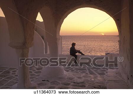 Stock Image -  sunset, Paros, Greek Islands, Parikia, Cyclades, Greece, Europe, Woman watching the sunset over the Aegean Sea from the terrace of a whitewashed church in the town of Parikia on Paros Island.. Fotosearch